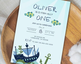 Peut inclure: Une invitation bleu clair avec le texte "OLIVER IS O-FISH-ALLY ONE". La carte comprend des illustrations de poissons, d'un navire et d'une ancre. L'invitation est pour une célébration le 13 juillet à 14h. Les informations RSVP sont incluses.
