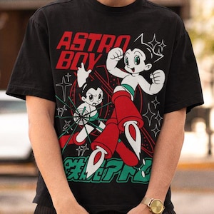 May include: Black t-shirt featuring a graphic of Astro Boy in red, white, and green. The text "ASTRO BOY" is in red, with Japanese characters below the illustration. The shirt is short-sleeved.