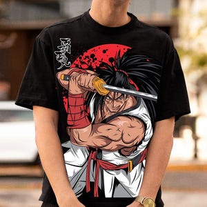 May include: Black t-shirt featuring a detailed illustration of a samurai warrior holding a katana sword against a red sun background. The warrior is depicted in a white and red outfit with long black hair. Japanese text is on the upper left.