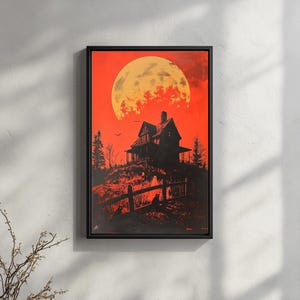 May include: A framed art print depicts a spooky scene with a large orange moon in a red sky. A silhouetted house sits atop a hill, with a fence and cats in the foreground. The artwork has a Halloween theme.