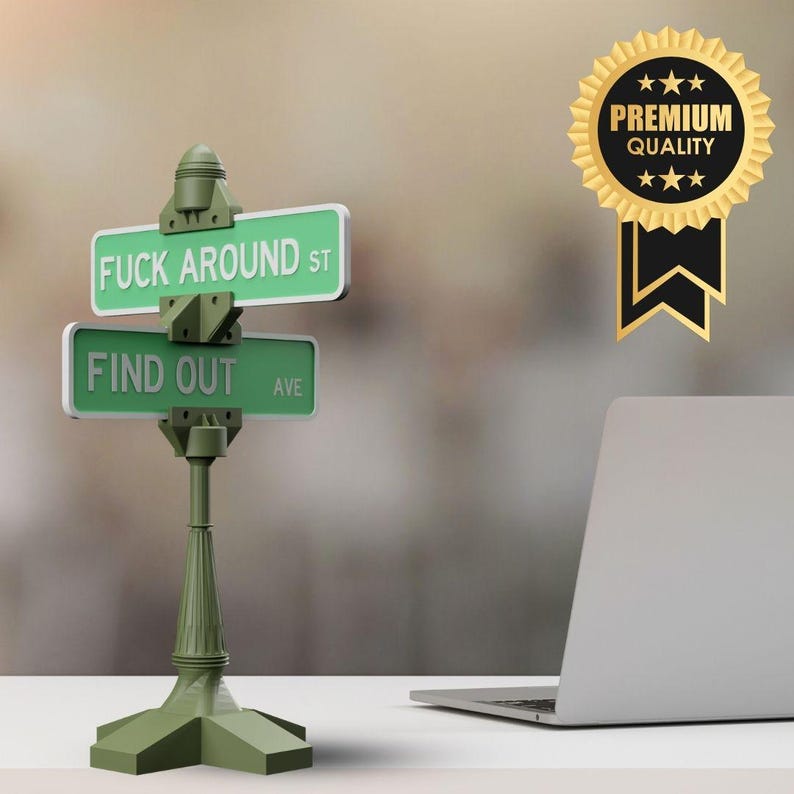 May include: A green street sign with the phrases "FUCK AROUND ST" and "FIND OUT AVE" in white text. The sign is mounted on a green post. A gold and black "PREMIUM QUALITY" badge is also visible.