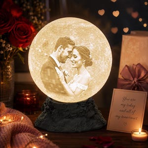 May include: A spherical moon lamp featuring a custom 3D-printed portrait of a couple in wedding attire. The lamp emits a warm glow and rests on a dark, textured, rock-like base. A card nearby displays the text: You are my today and all of my tomorrows.