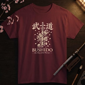 Può includere: T-shirt bordeaux con un design in stile giapponese. La maglietta presenta la parola "Bushido" e caratteri giapponesi sopra una spada e un motivo floreale. Il testo "The Way of the Warrior" è sotto.