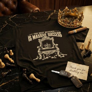 May include: Black t-shirt with the text "THE BEST REVENGE IS MASSIVE SUCCESS" and a graphic of a throne with a crown. Chess pieces, a gold crown, a cigar, and a note that says "Thank you for doubting me" are also present.