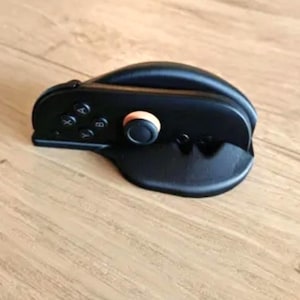 Op de afbeelding: Zwarte gamecontroller met een oranje knop en richtingknoppen. De controller ligt op een houten oppervlak. De controller heeft de letters A, B, X en Y op de knoppen.