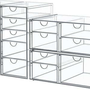 May include: Clear acrylic storage drawers with silver metal frames. The drawers have curved handles and are stacked in various configurations, offering versatile organization solutions. The design is modern and minimalist, suitable for various storage needs.