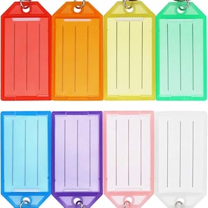 May include: A collection of eight keychains with clear plastic tags in various colors: red, orange, yellow, green, blue, purple, pink, and white. Each tag has vertical lines for writing and a silver metal ring.