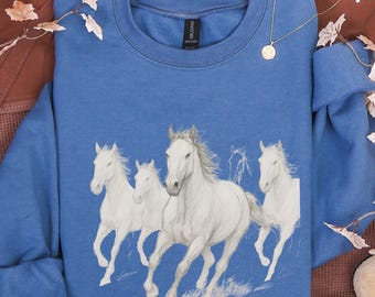 May include: A blue crewneck sweatshirt featuring a graphic print of four white horses running. The horses are depicted in a sketch-like style with flowing manes. The sweatshirt has long sleeves and a ribbed neckline, with a black brand label visible.