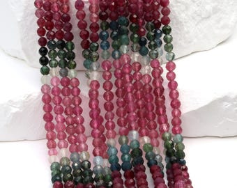 May include: Strands of faceted tourmaline beads in shades of pink, green, and blue. The beads are strung together, creating a cascading effect. The gemstones have a polished, reflective surface, and are displayed against a white background.