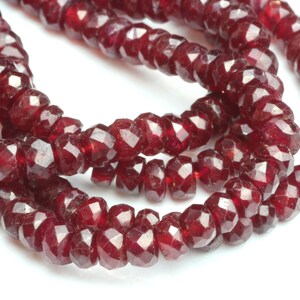 May include: Strands of faceted, deep red gemstone beads. The beads are strung together, creating a necklace or bracelet. The gemstones have a sparkling, polished appearance, reflecting light. The beads are a rich, dark red color.