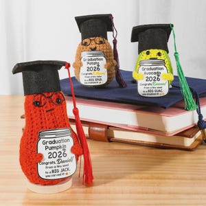 May include: Three handmade graduation-themed plush figures: a pumpkin, a potato, and an avocado, each wearing a black graduation cap. The pumpkin is red, the potato is tan, and the avocado is green. Each holds a sign with a graduation message.