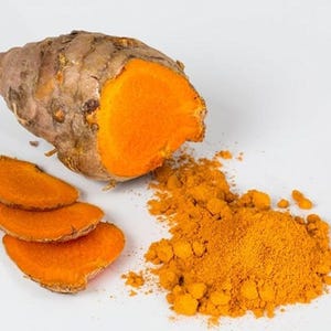 Puede incluir: Primer plano de raíz de cúrcuma, cortada y en polvo. La raíz de cúrcuma es marrón por fuera y de color naranja brillante por dentro. Tres rodajas de cúrcuma están junto a la raíz, y un montón de polvo de cúrcuma naranja está a la derecha.