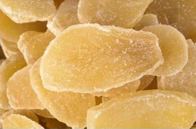 May include: Close-up of a pile of candied ginger slices. The ginger pieces are a light yellow color with a crystallized sugar coating. The texture appears slightly rough and uneven.