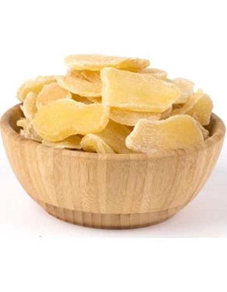 May include: A wooden bowl filled with dried ginger slices. The ginger has a light yellow color and a slightly translucent appearance. The bowl is made of light-colored wood and has a simple, natural design. The background is plain white.