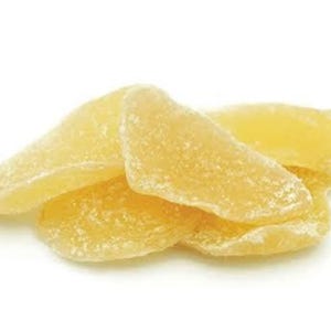 May include: A pile of candied ginger slices. The ginger pieces are a light yellow color and have a crystallized sugar coating. The slices are arranged in a loose pile against a white background.