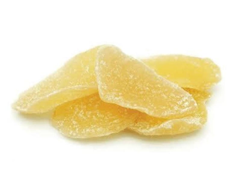 May include: A pile of candied ginger slices. The ginger pieces are a light yellow color and have a crystallized sugar coating. The slices are arranged in a loose pile against a white background.