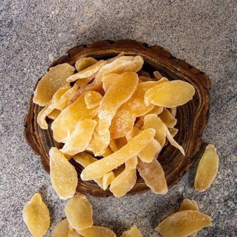 May include: A close-up shot of candied ginger slices, showcasing their golden-yellow color and crystallized sugar coating. The ginger is arranged in a rustic wooden bowl, set against a textured gray surface. The image highlights the texture and color of the ginger.