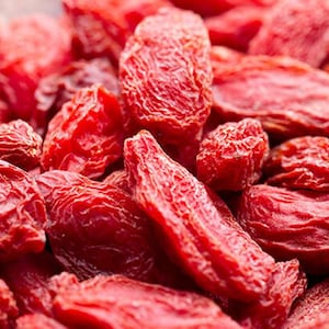 May include: A close-up shot of a heap of dried goji berries. The berries are a rich red hue and have a wrinkled appearance. They are clustered together, filling the frame. The image is well-lit, emphasising the colour and texture of the berries.