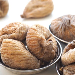 May include: A close-up shot of dried figs, displaying their wrinkled, tan skin and soft texture. The figs are presented in small, silver bowls, with some scattered around. The image emphasises the natural, organic look of the fruit.