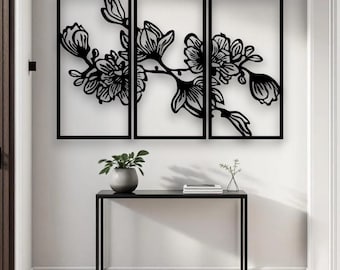 May include: Black metal floral wall art in a triptych design. The artwork features a detailed silhouette of a flowering branch with blossoms and buds. The piece is displayed on a white wall above a black console table.
