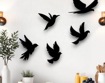 Puede incluir: Decoración de pared con cinco siluetas negras de pájaros en vuelo. Las aves con las alas extendidas crean una composición dinámica y decorativa en una pared blanca. Diseño sencillo y moderno para un interior contemporáneo.