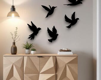 Puede incluir: Siluetas negras de pájaros en vuelo montadas en una pared clara. Un mueble de madera con diseño geométrico y una lámpara colgante están en primer plano. Un jarrón con una planta y dos pequeñas plantas en macetas están en el mueble.