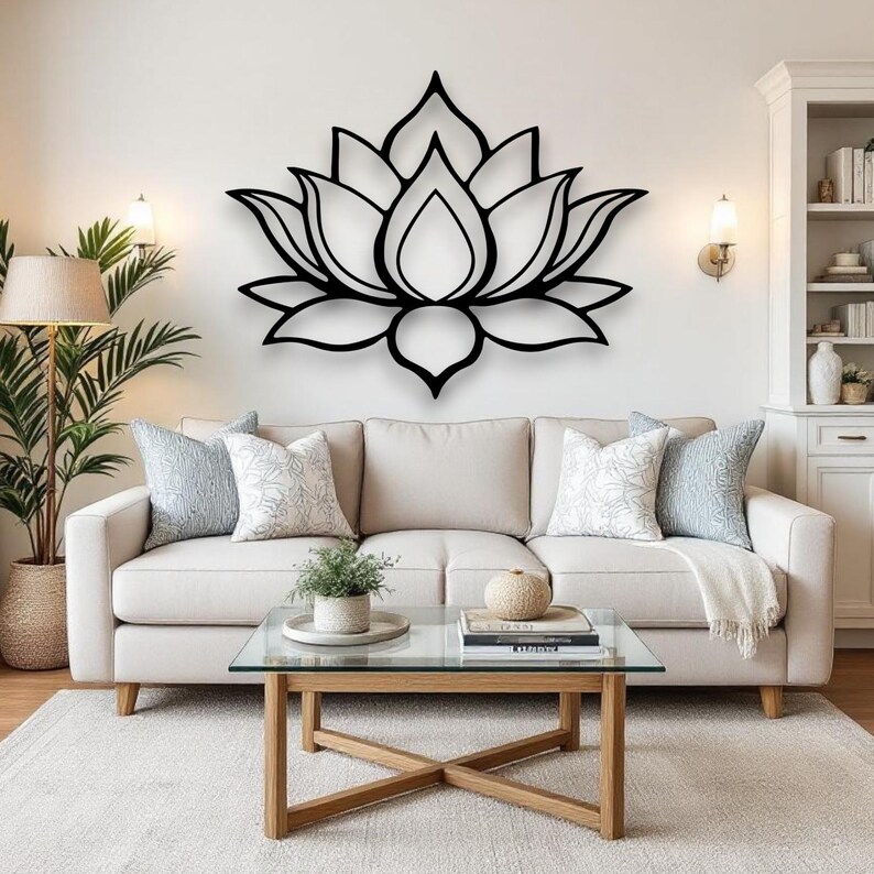 May include: A large, black metal lotus flower wall art decorates a white wall above a beige sofa. The living room features a glass-top coffee table, decorative pillows, and a potted plant.