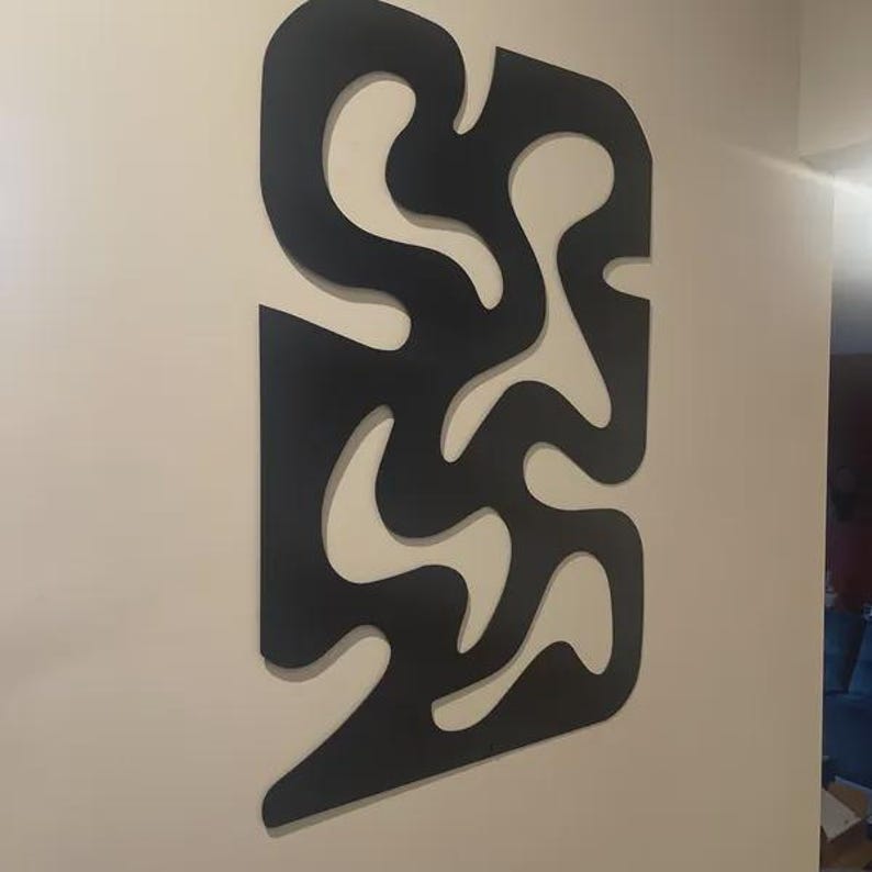 K&ouml;nnte beinhalten: Ein gro&szlig;es, schwarzes, flaches Wandkunstobjekt mit einer abstrakten, durchgehenden, geschwungenen Form und mehreren Ausschnitten, die die dahinterliegende Wand freigeben. Das Design besteht aus miteinander verbundenen, organischen Kurven.