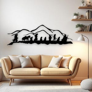 Può includere: Arte murale in metallo nero raffigurante una silhouette di un gruppo di figure che camminano attraverso un paesaggio montuoso. L'opera d'arte è montata sopra un divano beige in un soggiorno.