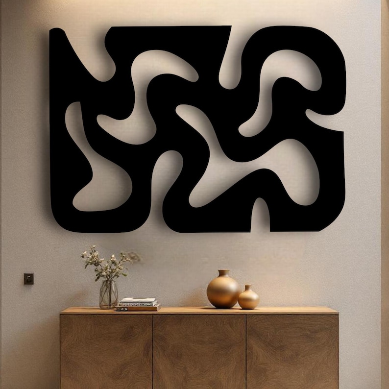 K&ouml;nnte beinhalten: Ein gro&szlig;es schwarzes Wandkunstobjekt mit einem durchgehenden, flie&szlig;enden und abstrakten Ausschnittdesign mit organischen, geschwungenen Formen. Das Kunstwerk ist an einer schlichten Wand &uuml;ber einem Holzschrank mit zwei Goldvasen und B&uuml;chern montiert.