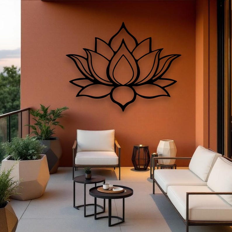 May include: A black metal lotus flower wall art decorates an outdoor patio with white furniture and potted plants. The wall is painted a warm orange color, creating a relaxing atmosphere.