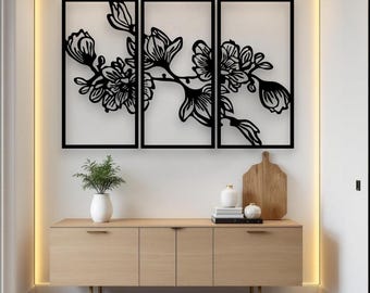 May include: Black floral wall art in a triptych arrangement. The artwork features a stylized branch with flowers and buds, set against a white background. The frames are black. A wooden cabinet with decor sits below the art.