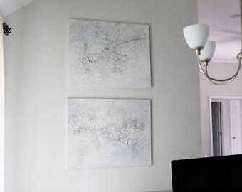 Könnte beinhalten: Zwei quadratische abstrakte Gemälde mit strukturierten weißen und grauen Oberflächen sind an einer hellgrauen Wand angebracht. Die Gemälde haben eine moderne, minimalistische Ästhetik und verleihen der Inneneinrichtung einen Hauch zeitgenössischer Kunst.