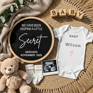 May include: A pregnancy announcement featuring a white baby onesie with the name "Wilson" and a red heart, a letter board with the text "Secret", a teddy bear, baby socks, ultrasound image, and wooden blocks spelling "BABY".