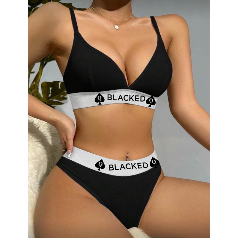 K&ouml;nnte beinhalten: Schwarzes Dessous-Set mit einem Triangel-BH und passendem Slip. Der BH und der Slip haben ein wei&szlig;es Band mit dem Wort "BLACKED" und einem Pik-Symbol. Das Set ist aus einem weichen, bequemen Material gefertigt.