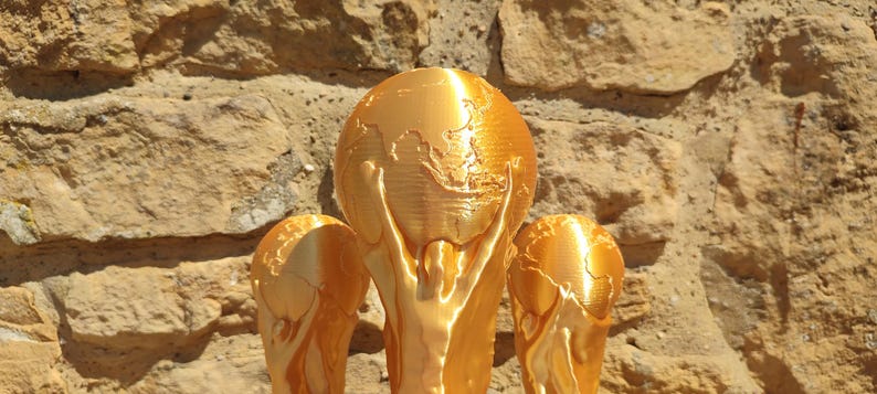 Puede incluir: Un trofeo dorado con un dise&ntilde;o de globo terr&aacute;queo sostenido por dos figuras. El trofeo est&aacute; sobre un muro de piedra texturizado. El trofeo es un s&iacute;mbolo de logro.