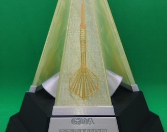 Könnte beinhalten: Trophäe mit pyramidenförmiger Spitze und Dart-Design im Inneren. Der Sockel ist schwarz mit dem Text "GDA PREMIER LEAGUE". Die Trophäe steht vor einem grünen Hintergrund.
