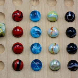 Peut inclure: Un plateau de jeu en bois avec 19 trous et 16 billes. Les billes sont rouges, bleues, noires et blanches avec des tourbillons. Un seul dé avec des points verts et dorés est dans le coin supérieur gauche.