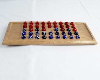 May include: A wooden board game with a rectangular oak tray. The game features red, white, and blue marbles arranged in rows. The marbles are a mix of solid red, white swirl, and blue swirl designs.
