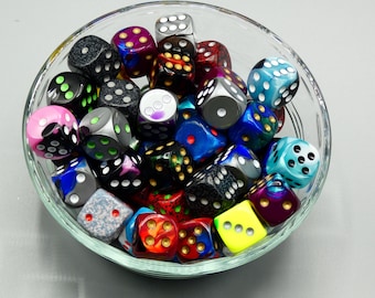 May include: A clear glass bowl filled with a variety of colorful dice. The dice are in various colors, including black, blue, pink, and yellow, with white or colored pips. The dice are of standard size, suitable for tabletop games.