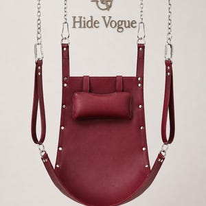 May include: A burgundy leather swing with silver-tone hardware and a small headrest. The swing is suspended from chains and features the text "Hide Vogue" in a silver-tone logo.