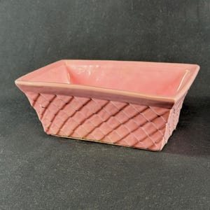 May include: A rectangular, pink ceramic basket-style planter. The planter has a woven basket design on the sides and a smooth, solid pink interior. The rim is a darker shade of pink.