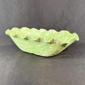 May include: An oval-shaped ceramic bowl featuring a vibrant lime green base color with a delicate, white, web-like or lace-inspired pattern overlay. The bowl has a distinctively wavy, ruffled edge that creates a scalloped rim around the top.