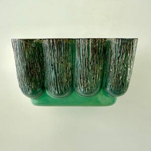 May include: A rectangular, ceramic planter with a textured, vertical stripe design. The planter has a light green base and a darker green and black upper section. The planter's shape is reminiscent of a series of connected arches.