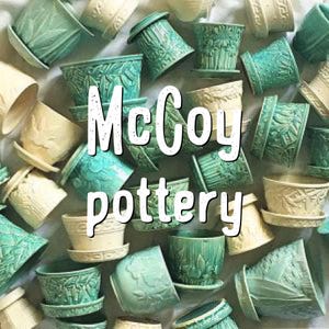 May include: An assortment of vintage McCoy pottery planters in various shapes and sizes. The planters are in shades of green and cream, with embossed floral and geometric designs. The text "McCoy pottery" is overlaid on the image.