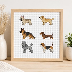 May include: A square wooden frame containing a cross-stitch embroidery on white Aida cloth. The design features six distinct dog breeds arranged in two columns: a French Bulldog, a Golden Retriever, a German Shepherd, a Dachshund, a Poodle, and a Beagle.