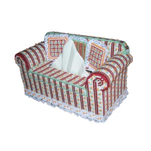 Könnte beinhalten: Eine dekorative Taschentuchbox-Abdeckung in Form eines Miniatursofas. Die Abdeckung besteht aus Kunststoff-Leinwand mit einem gestreiften Muster in Rot, Weiß und Orange. Sie hat gerollte Armlehnen und dekorative Kissen. Weiße Taschentücher sind sichtbar.