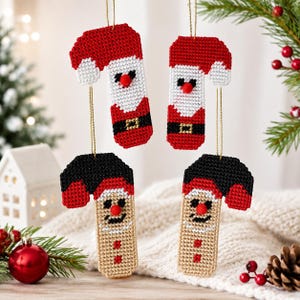 May include: Four hanging ornaments crafted from plastic canvas with cross-stitch detailing. Two ornaments feature a red and white Santa Claus design with a black belt, while two feature a black and tan elf design with red accents and a red nose.