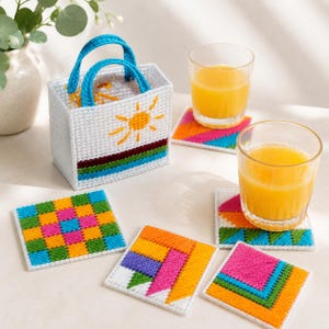 May include: A white plastic canvas tote bag with blue handles and a sun design, next to colorful square coasters and two glasses of orange juice. The coasters have geometric patterns in various colors.