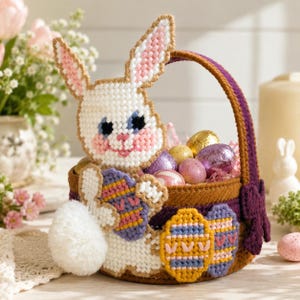May include: A handcrafted Easter basket featuring a white bunny with pink-lined ears and a fluffy tail. The basket is filled with colorful Easter eggs, including gold, purple, and pink foil-wrapped chocolate eggs. The basket is decorated with embroidered egg designs.